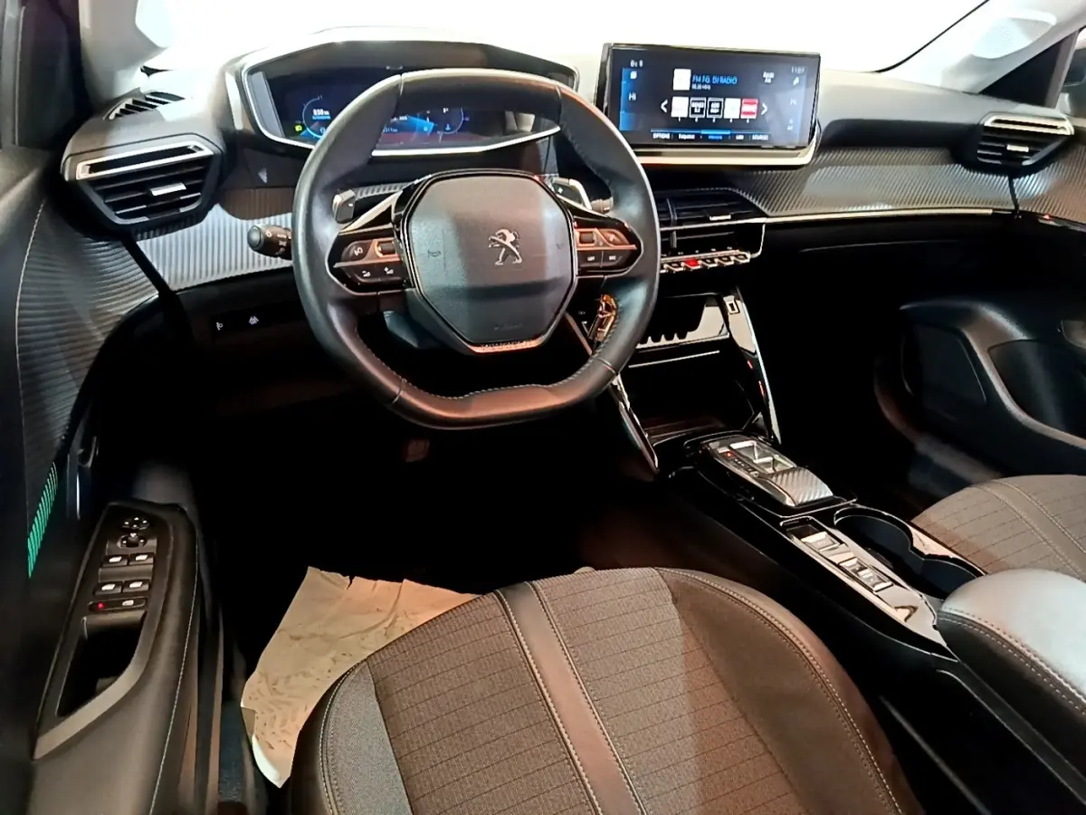 Vue intérieure avant de la Peugeot 208 2023, tableau de bord moderne avec écran tactile et volant cuir multifonctions.