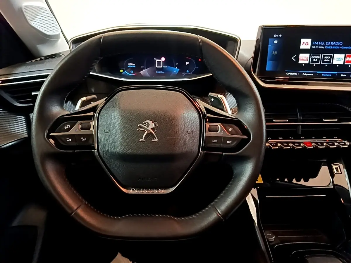 Vue rapprochée du volant cuir noir de la Peugeot 208 avec tableau de bord numérique et écran tactile central.