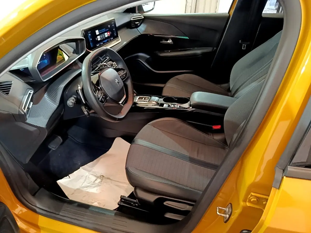 Intérieur côté conducteur d'une Peugeot 208 jaune 2023, montrant le volant cuir multifonctions et l'écran tactile central.
