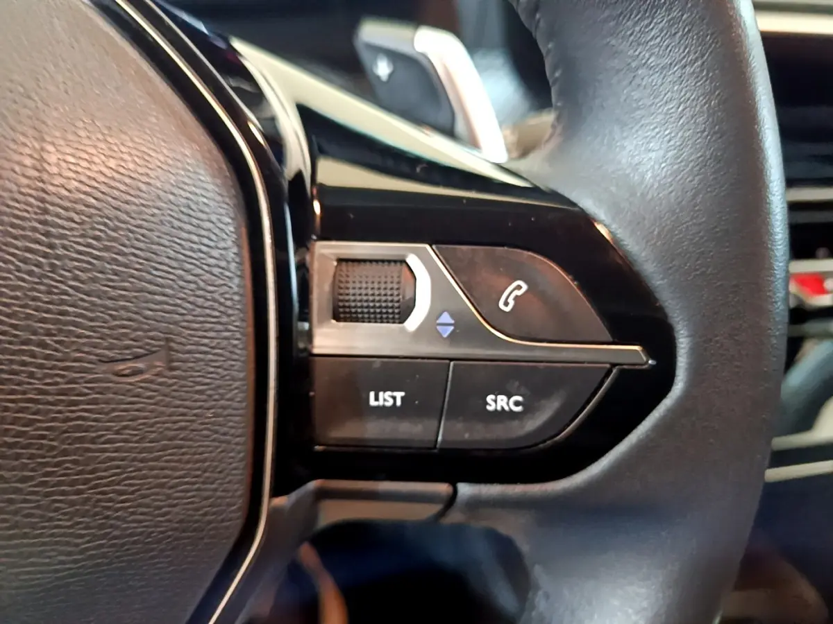 Gros plan sur les commandes gauche du volant cuir du Peugeot 208 2023, boutons de téléphone et sélection audio visibles.