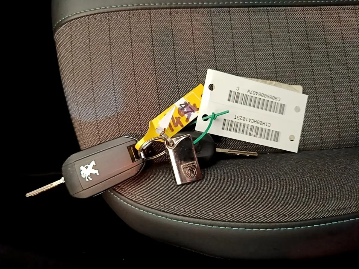 Gros plan sur une clé Peugeot posée sur un siège tissu gris avec surpiqûres bleues à l'intérieur d'une 208 jaune.