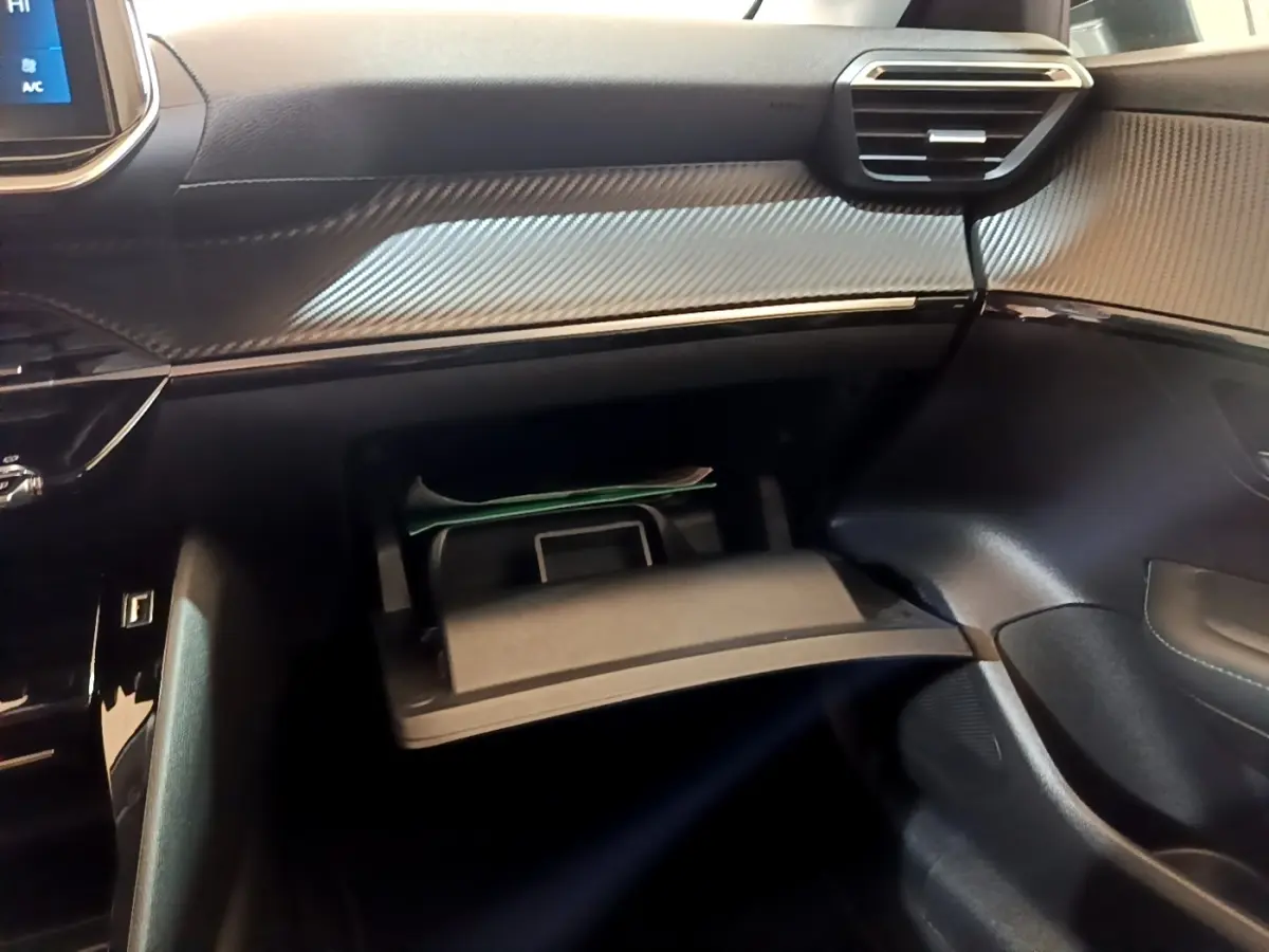 Vue intérieure côté passager de la Peugeot 208 2023 avec boîte à gants ouverte et tableau de bord noir texturé.