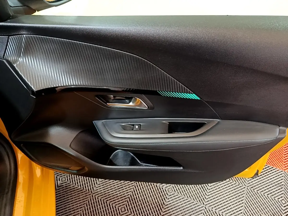 Vue intérieure côté gauche de la porte avant d'une Peugeot 208 jaune avec insert décoratif gris et poignée métallique.