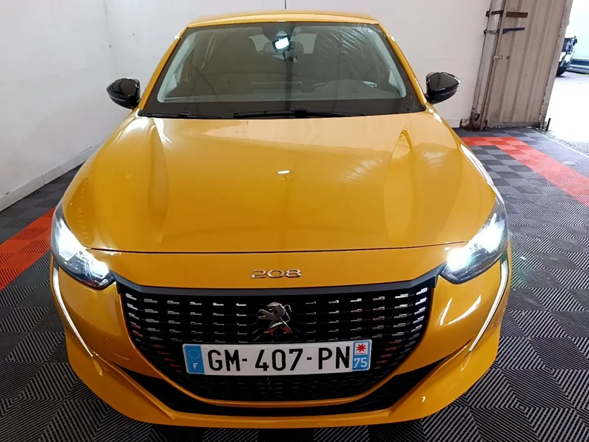 Vue avant d'une Peugeot 208 jaune 2023 avec phares LED allumés et calandre noire distinctive.