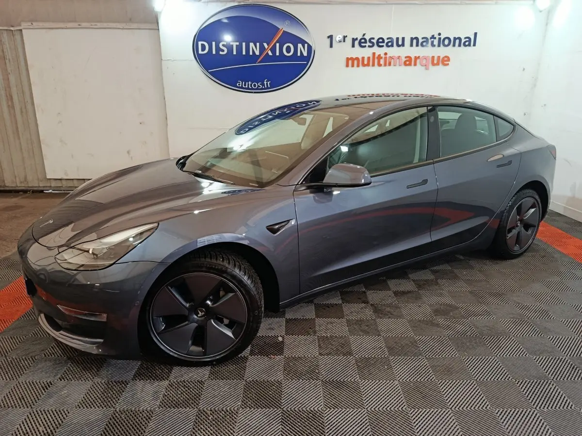 Tesla Model 3 Grande Autonomie gris foncé vue de côté droit en intérieur avec jantes noires et logo visible.