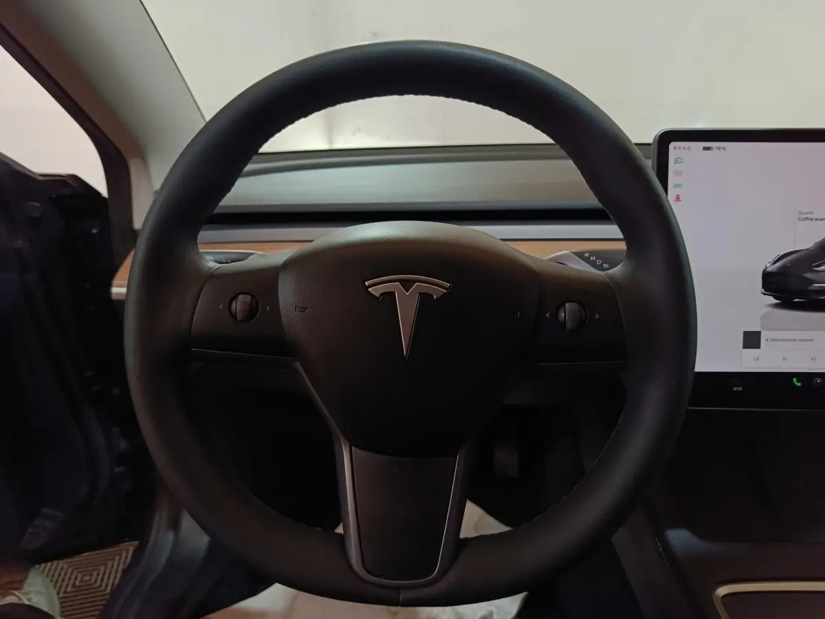 Vue rapprochée du volant noir de la Tesla Model 3 Grande Autonomie 2022 avec écran tactile central visible à droite.