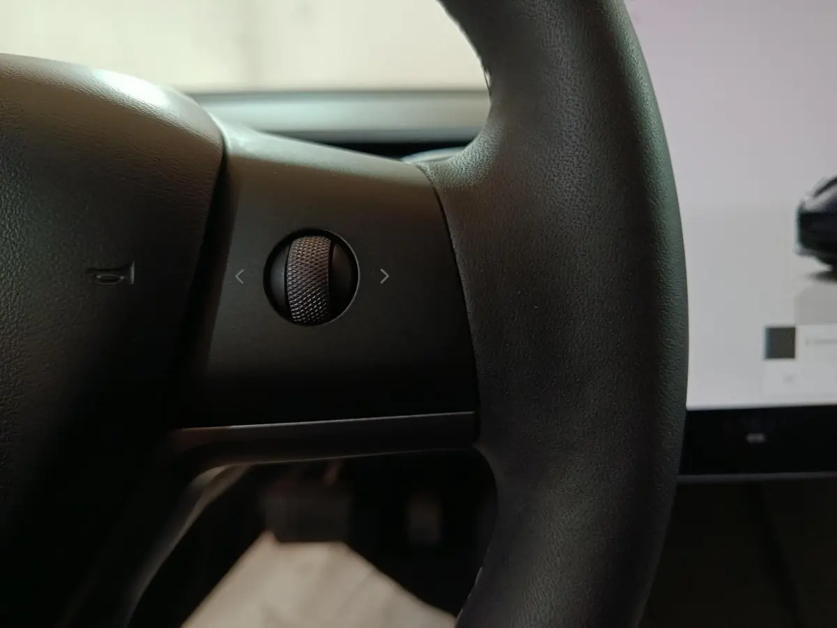Gros plan sur la molette de commande à gauche du volant noir dans l’habitacle d’une Tesla Model 3 gris foncé.