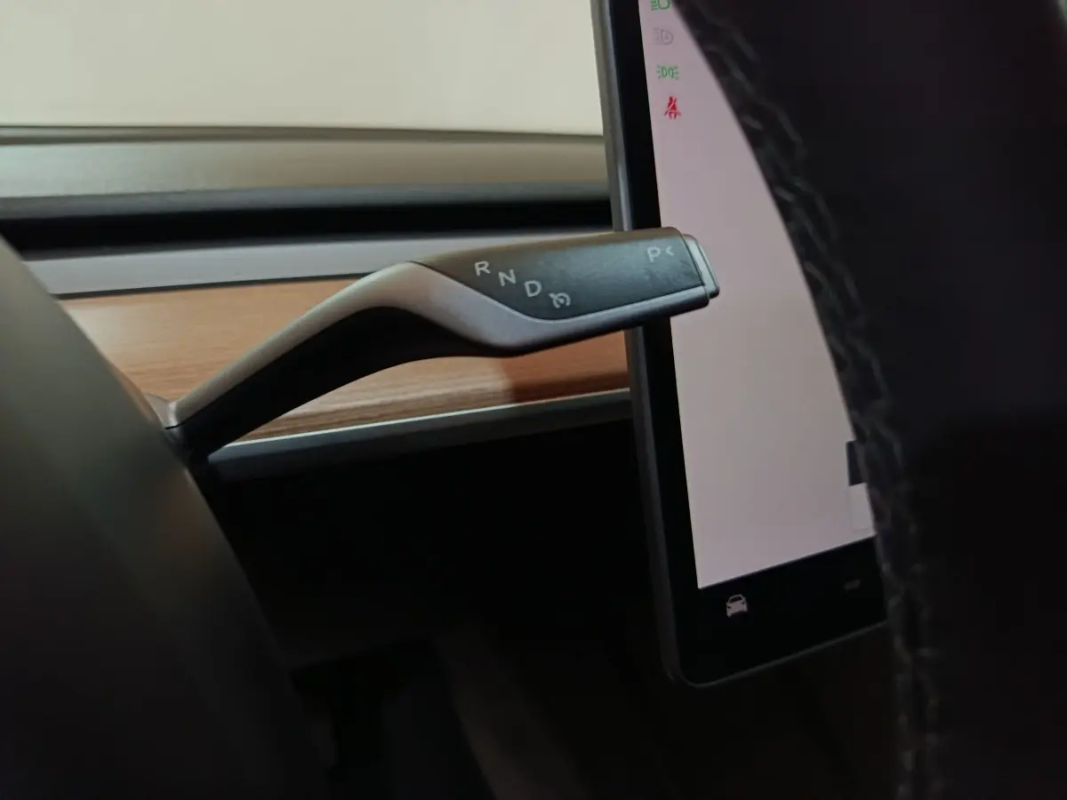 Gros plan sur le levier de vitesses noir et argenté à droite du volant dans l’habitacle gris foncé d’une Tesla Model 3 2022.