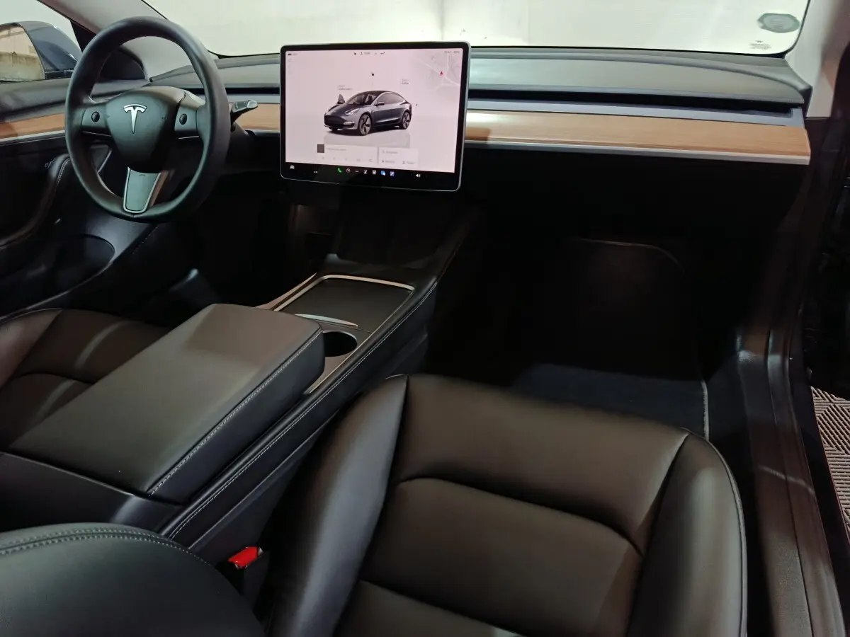 Intérieur avant de la Tesla Model 3 gris foncé, avec tableau de bord minimaliste et grand écran tactile central.