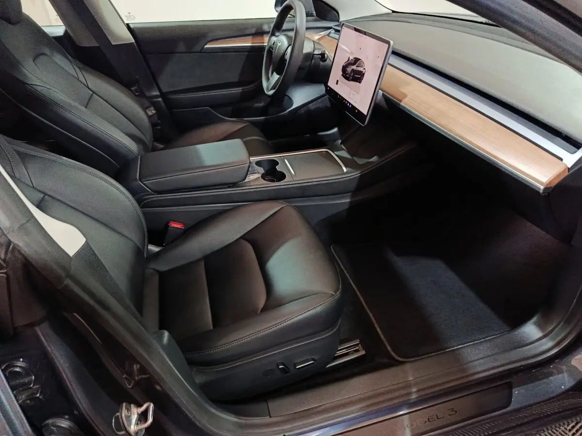 Intérieur Tesla Model 3 Grande Autonomie 2022 vu côté passager, sièges noirs et tableau de bord bois clair avec écran tactile central.