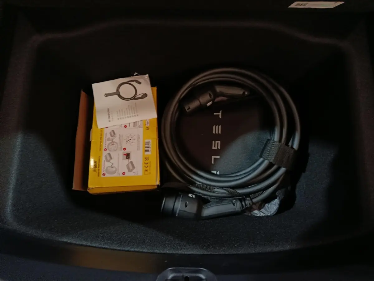 Vue intérieure du coffre d'une Tesla Model 3 gris foncé avec câble de charge et boîte jaune de rangement.
