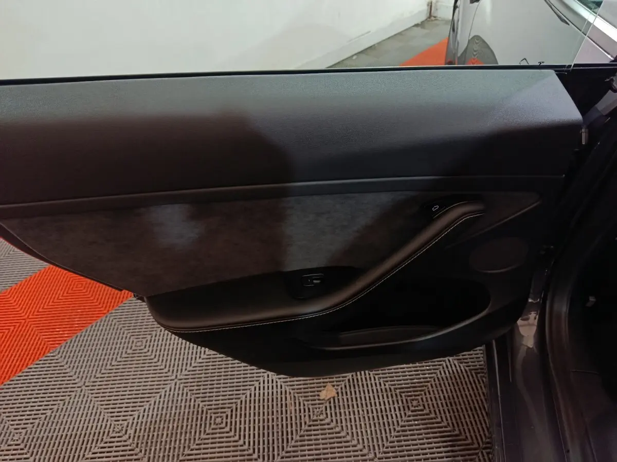 Gros plan sur la porte intérieure côté gauche d'une Tesla Model 3 gris foncé, avec garniture noire et bouton de vitre.