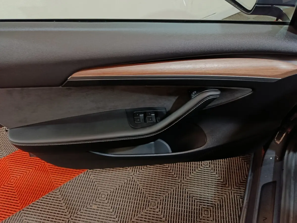 Vue intérieure côté gauche de la porte d’une Tesla Model 3 gris foncé avec garniture bois et commandes vitres.