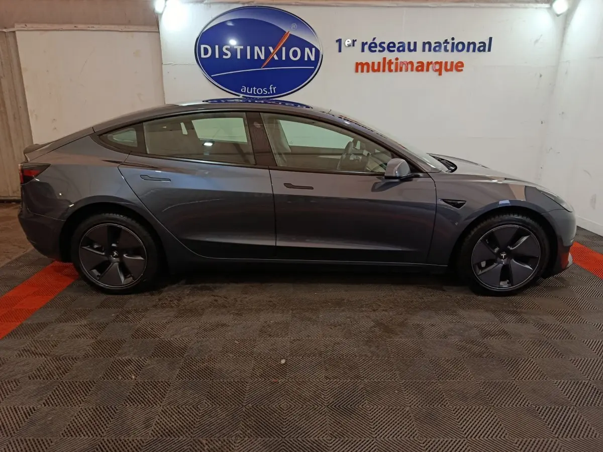 Profil droit d'une Tesla Model 3 Grande Autonomie gris foncé, avec jantes aérodynamiques et poignées affleurantes.