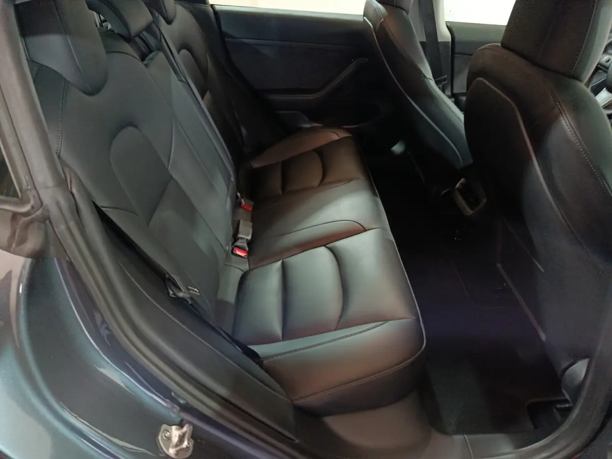 Vue intérieure côté arrière gauche montrant la banquette en cuir noir de la Tesla Model 3 Grande Autonomie gris foncé.