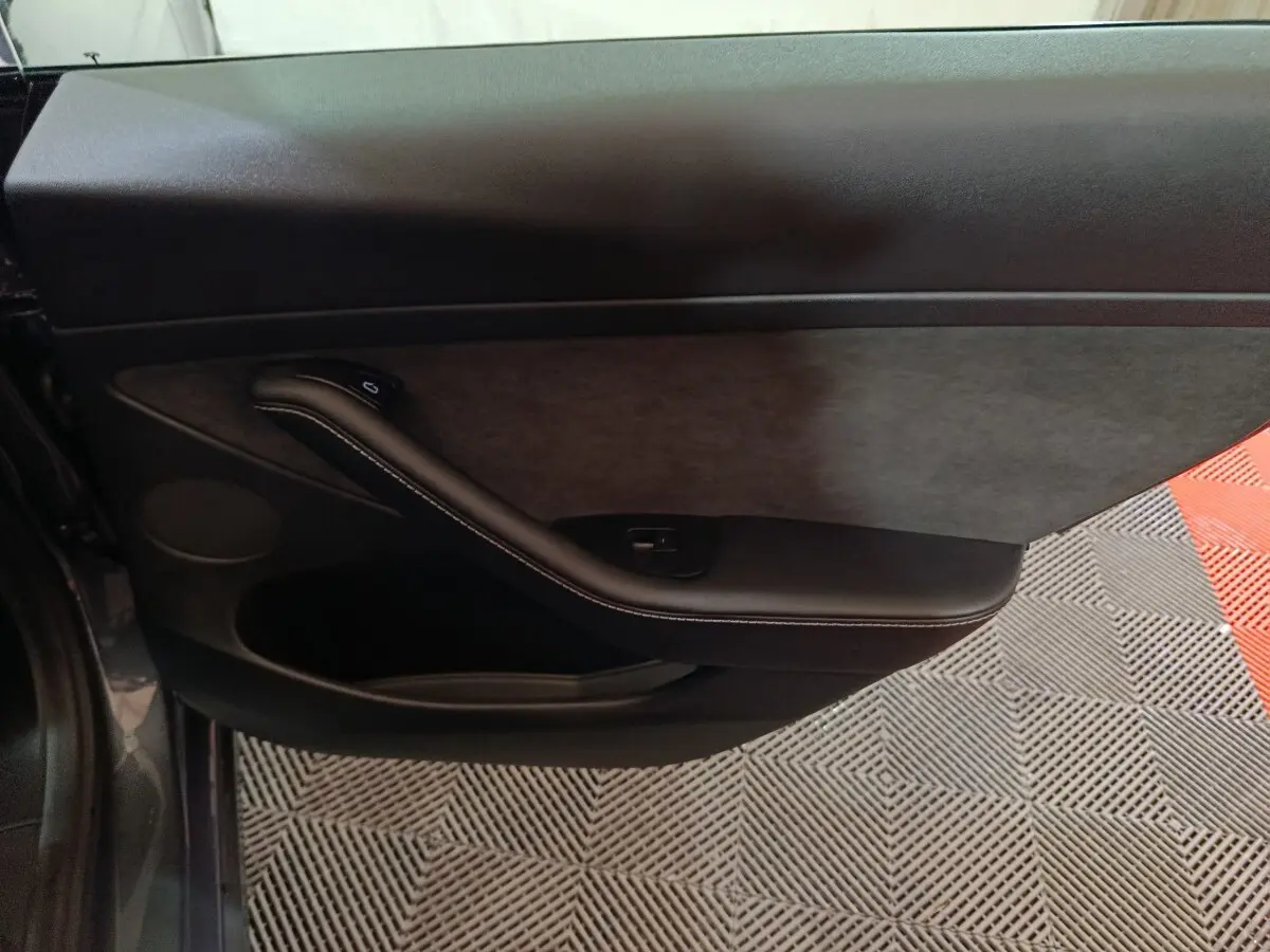 Vue intérieure du panneau de porte côté conducteur gris foncé de la Tesla Model 3 Grande Autonomie 2022 avec accoudoir et commande de vitre.