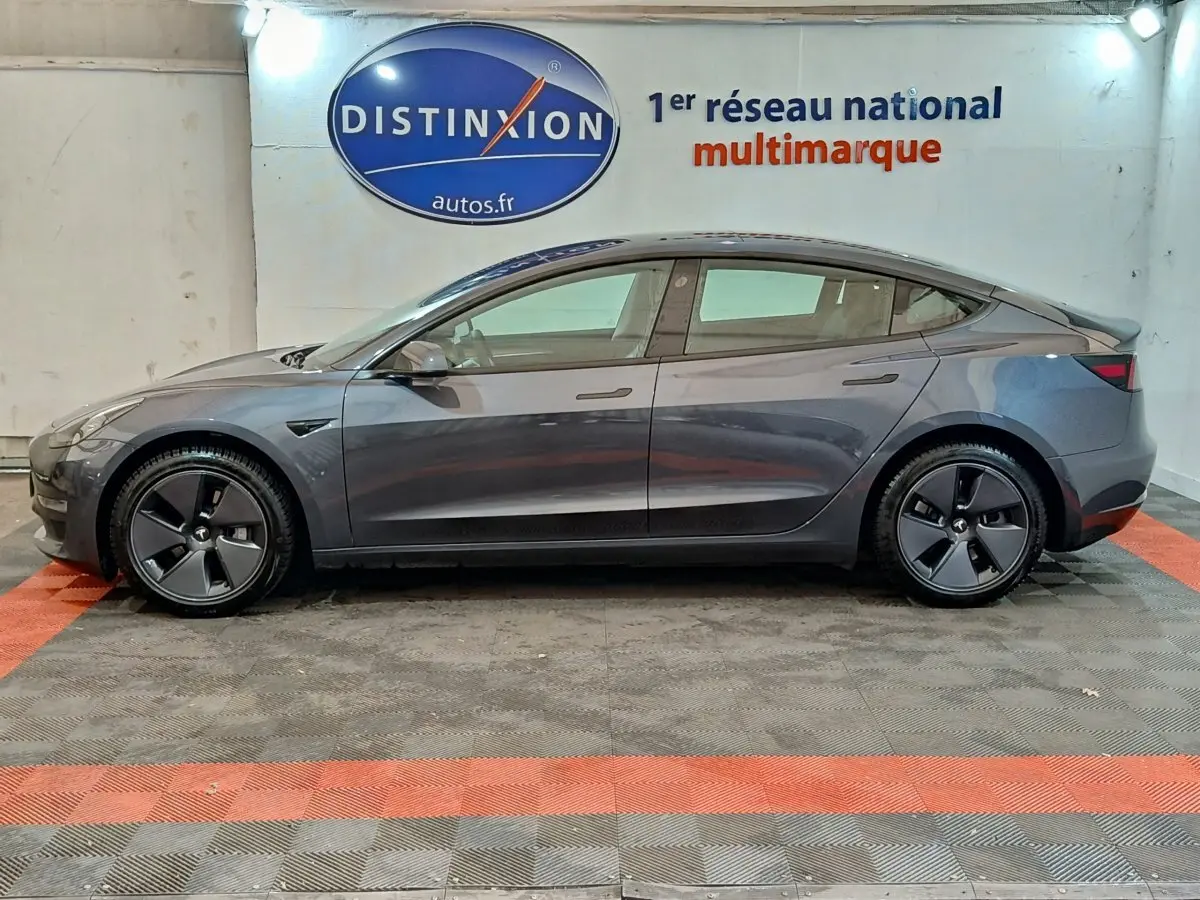 Vue latérale droite d'une Tesla Model 3 Grande Autonomie gris foncé, avec jantes aérodynamiques et logo distinctif.