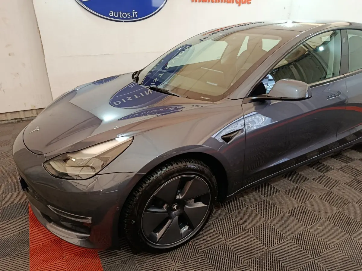 Vue 3/4 avant droit d'une Tesla Model 3 Grande Autonomie gris foncé avec jantes noires et phares LED.