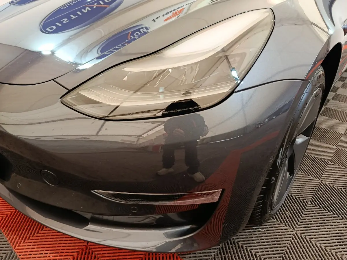 Gros plan sur l'avant droit gris foncé d'une Tesla Model 3 2022, mettant en valeur le phare LED et la jante noire.