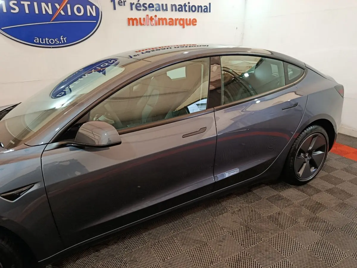 Profil côté gauche d'une Tesla Model 3 Grande Autonomie gris foncé, avec poignées affleurantes et jantes aérodynamiques.
