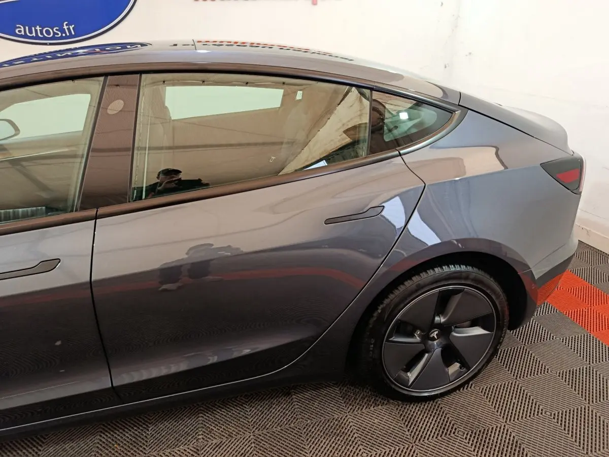 Vue latérale droite sur l'arrière d'une Tesla Model 3 gris foncé avec jante noire et poignées affleurantes.