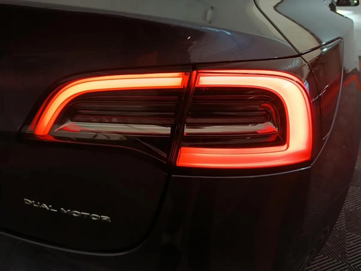 Gros plan sur le feu arrière droit rouge allumé d’une Tesla Model 3 Grande Autonomie gris foncé.