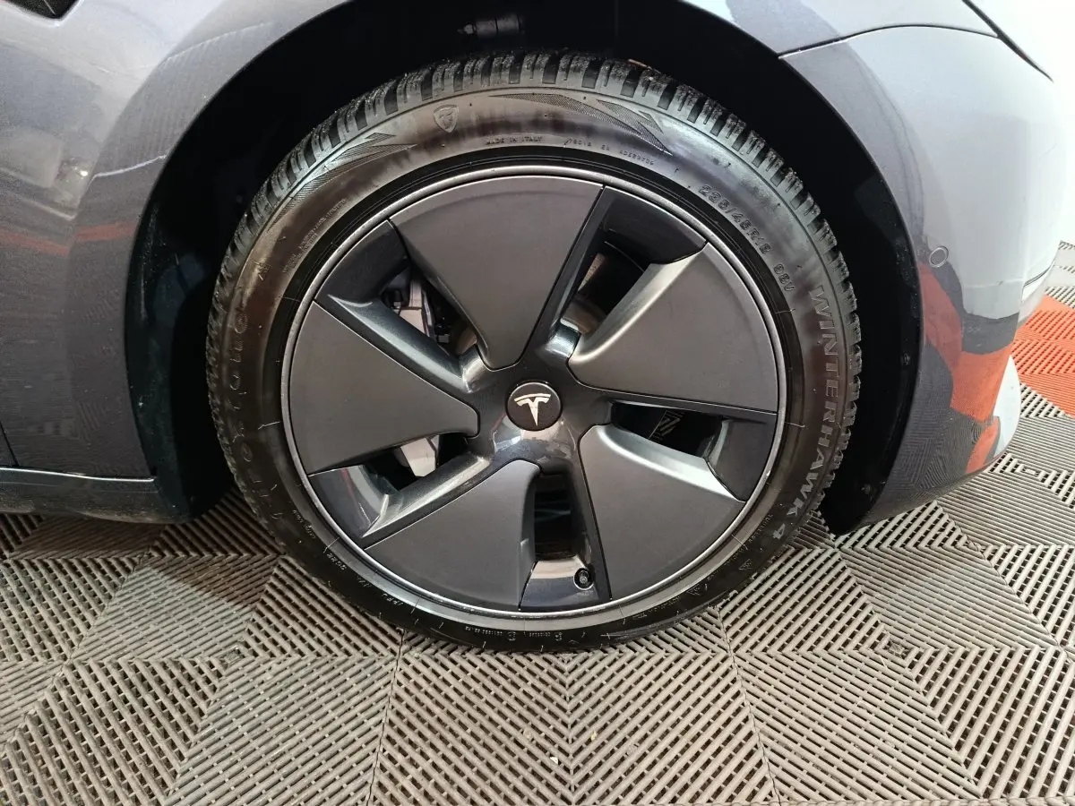 Gros plan sur la roue avant droite d’une Tesla Model 3 gris foncé avec jante aérodynamique.