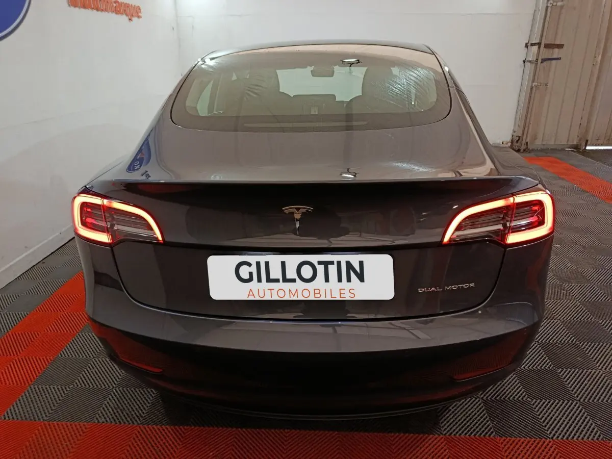 Vue arrière d'une Tesla Model 3 Grande Autonomie gris foncé avec feux LED allumés dans un garage.