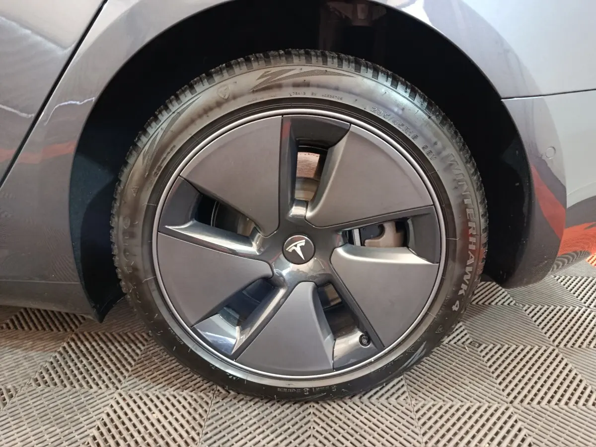 Vue rapprochée de la roue arrière droite d'une Tesla Model 3 gris foncé, montrant le passage de roue et le pneu Winterhawk 4.