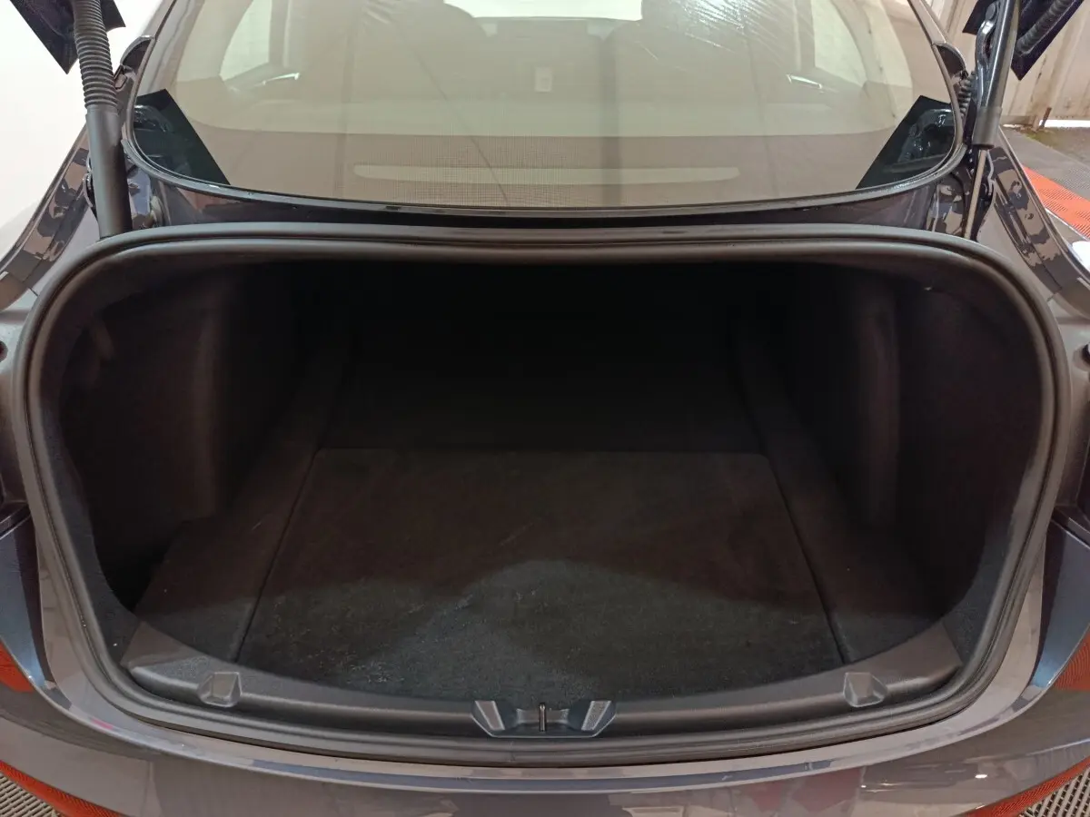 Coffre ouvert vu de l'arrière d'une Tesla Model 3 gris foncé, montrant l'espace de rangement vide.