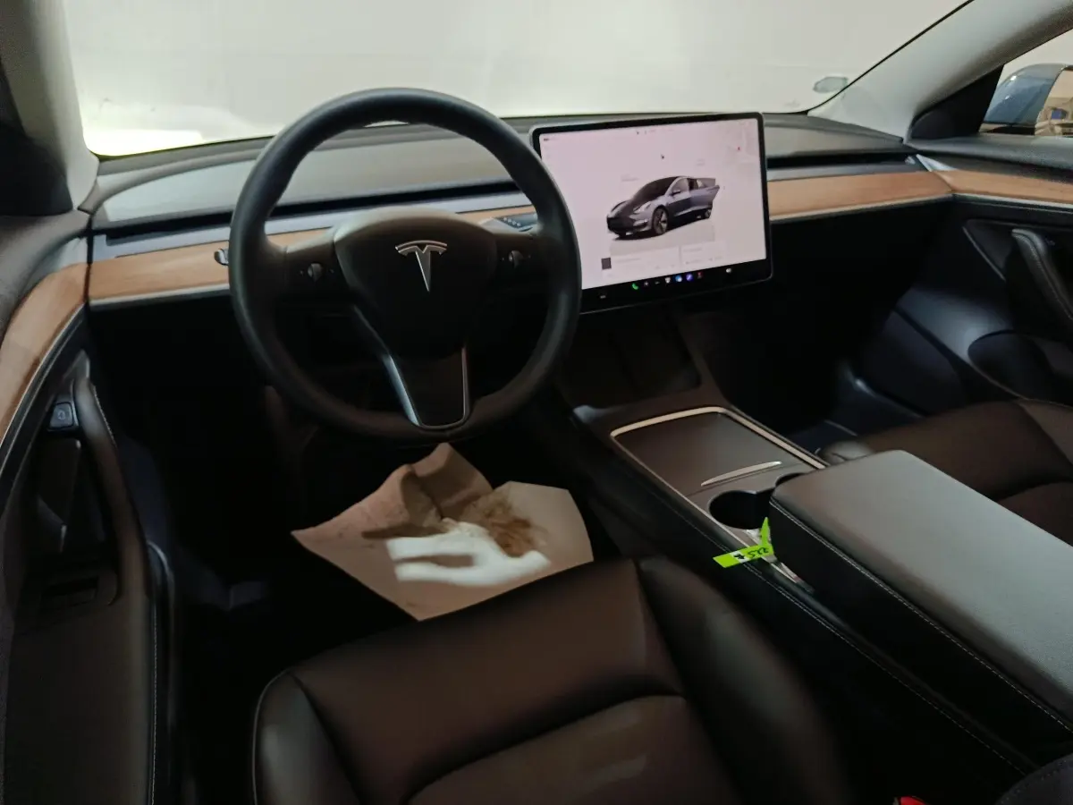 Intérieur noir de Tesla Model 3 2022, vue du poste de conduite avec écran tactile central et tableau de bord bois.