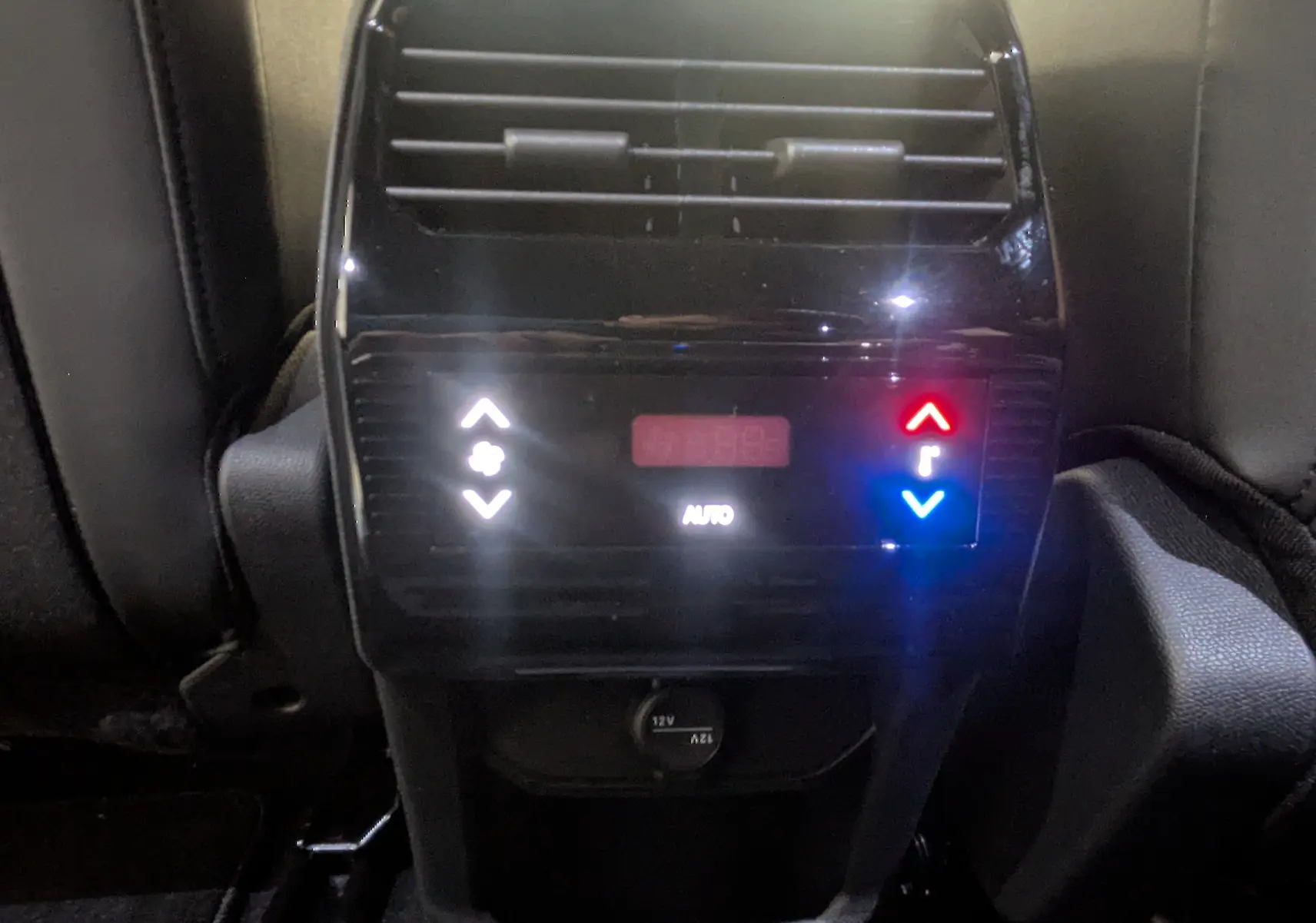 Détail de la console arrière noire avec commandes de climatisation automatique et prise 12V dans un Peugeot 5008 blanc.