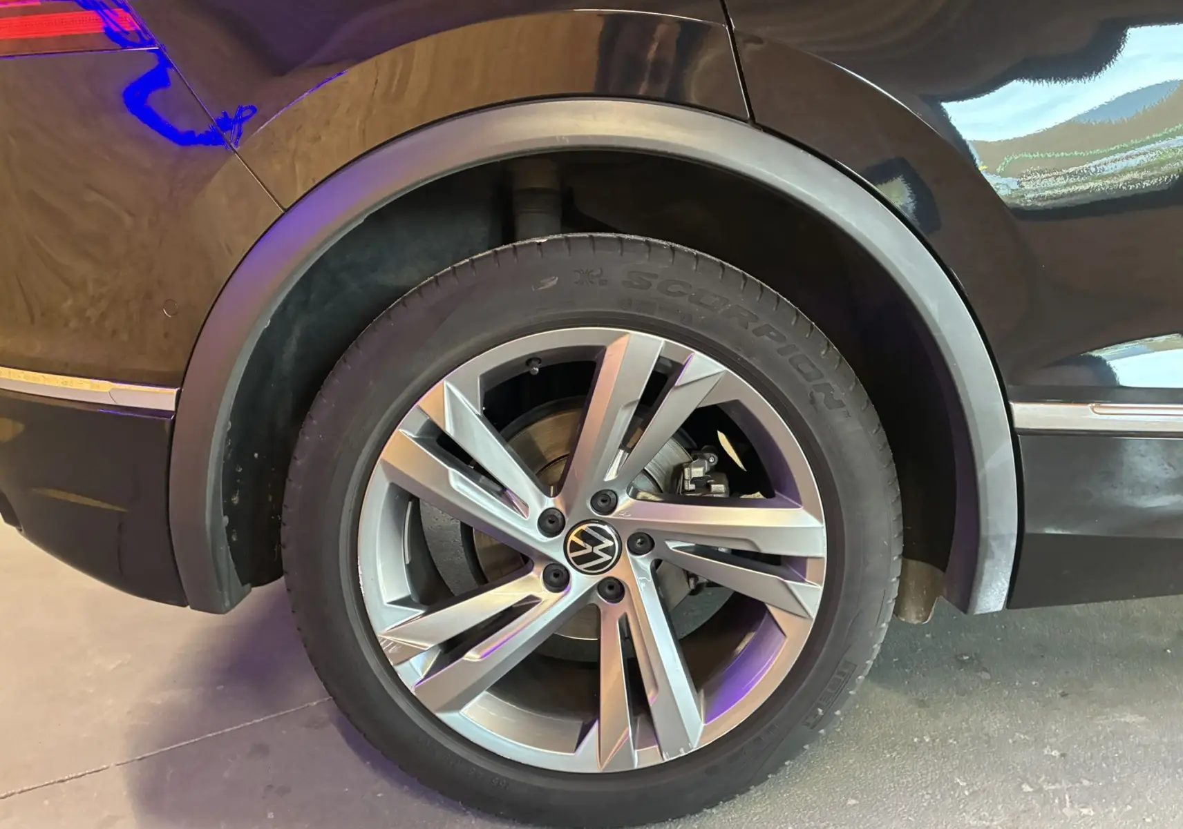 Gros plan sur la roue arrière droite du Volkswagen Tiguan noir avec jante alu et logo VW au centre.