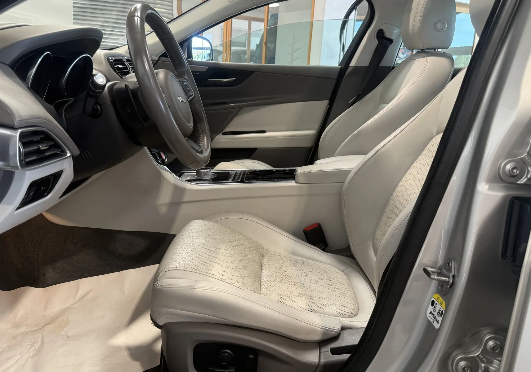 Intérieur beige clair de la Jaguar XE 20d Prestige 2015, vue côté conducteur avec tableau de bord et sièges en cuir.