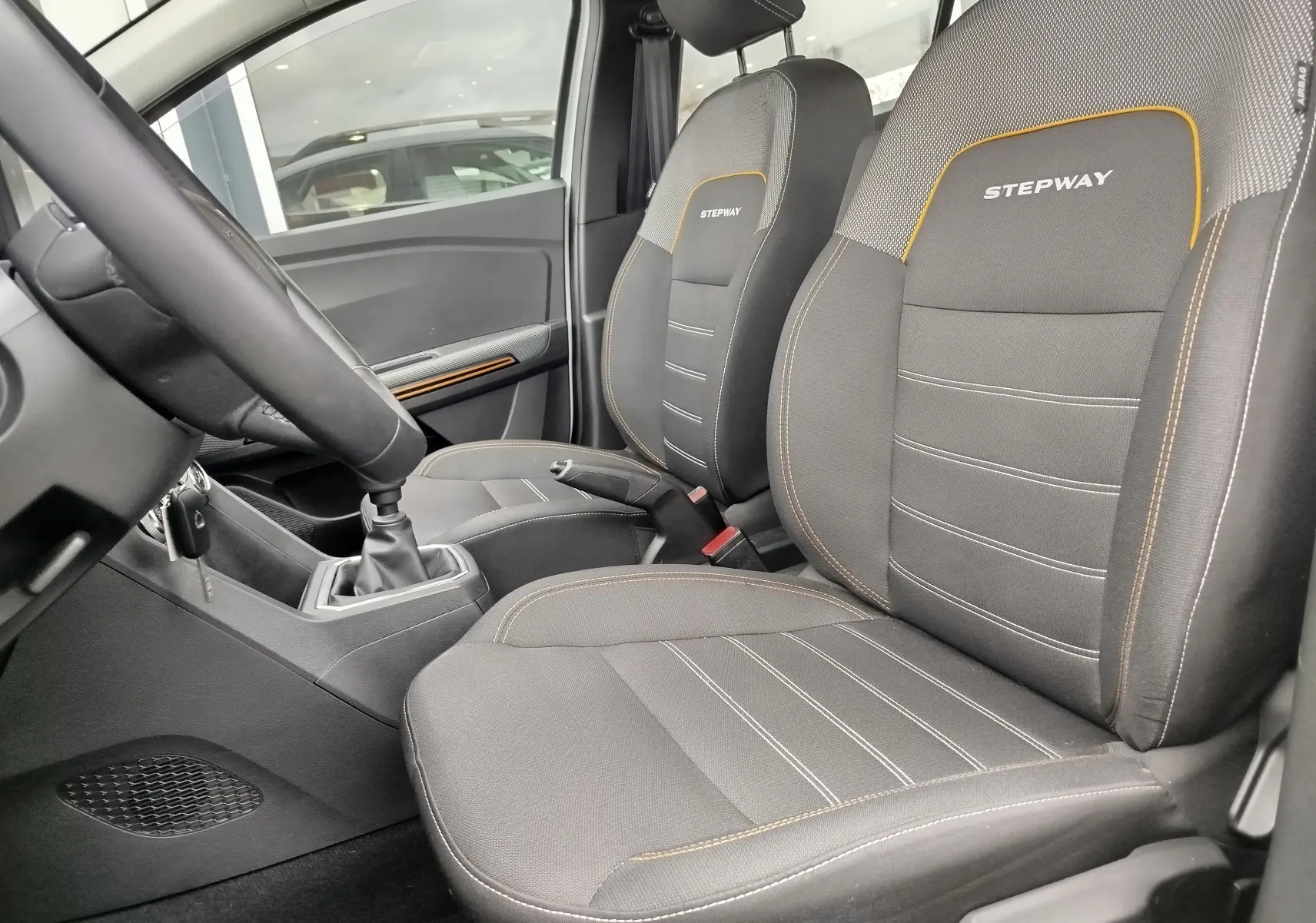 Intérieur de la Dacia Sandero Stepway 2021 vu côté conducteur, sièges gris avec surpiqûres orange et logo Stepway brodé.