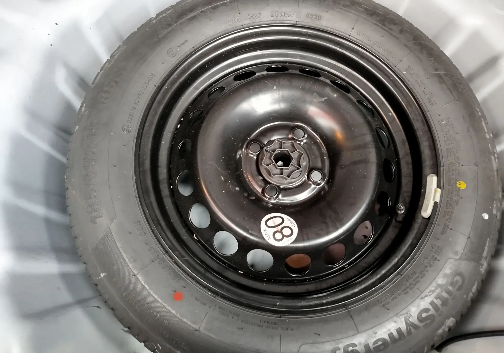 Pneu de secours noir avec jante acier circulaire, visible dans le coffre d'une Dacia Sandero Stepway blanche.