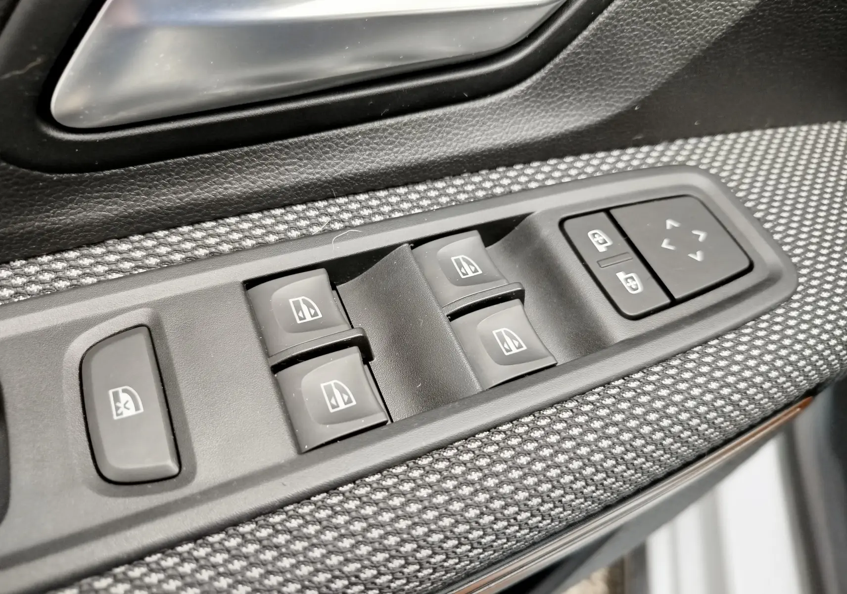 Gros plan sur les commandes de lève-vitres et réglage des rétroviseurs côté conducteur d'une Dacia Sandero Stepway 2021.