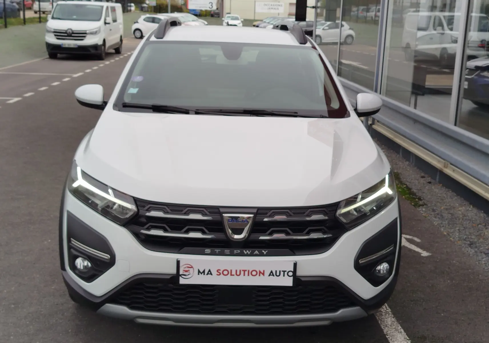Vue frontale d'une Dacia Sandero Stepway blanche glacier avec feux LED allumés et calandre noire marquée Stepway.