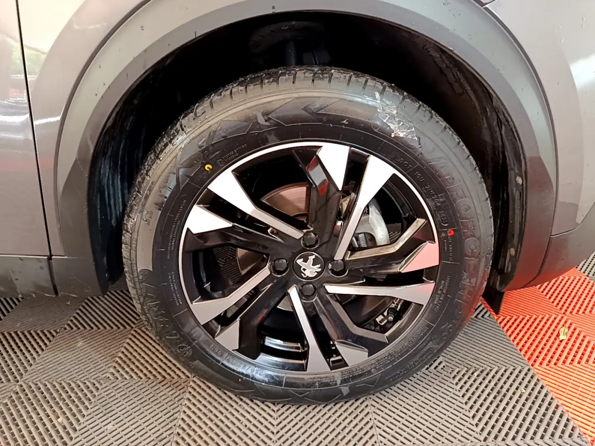 Gros plan sur la roue avant droite d’un Peugeot 2008 gris foncé, avec jante alliage noire et argentée au design moderne.