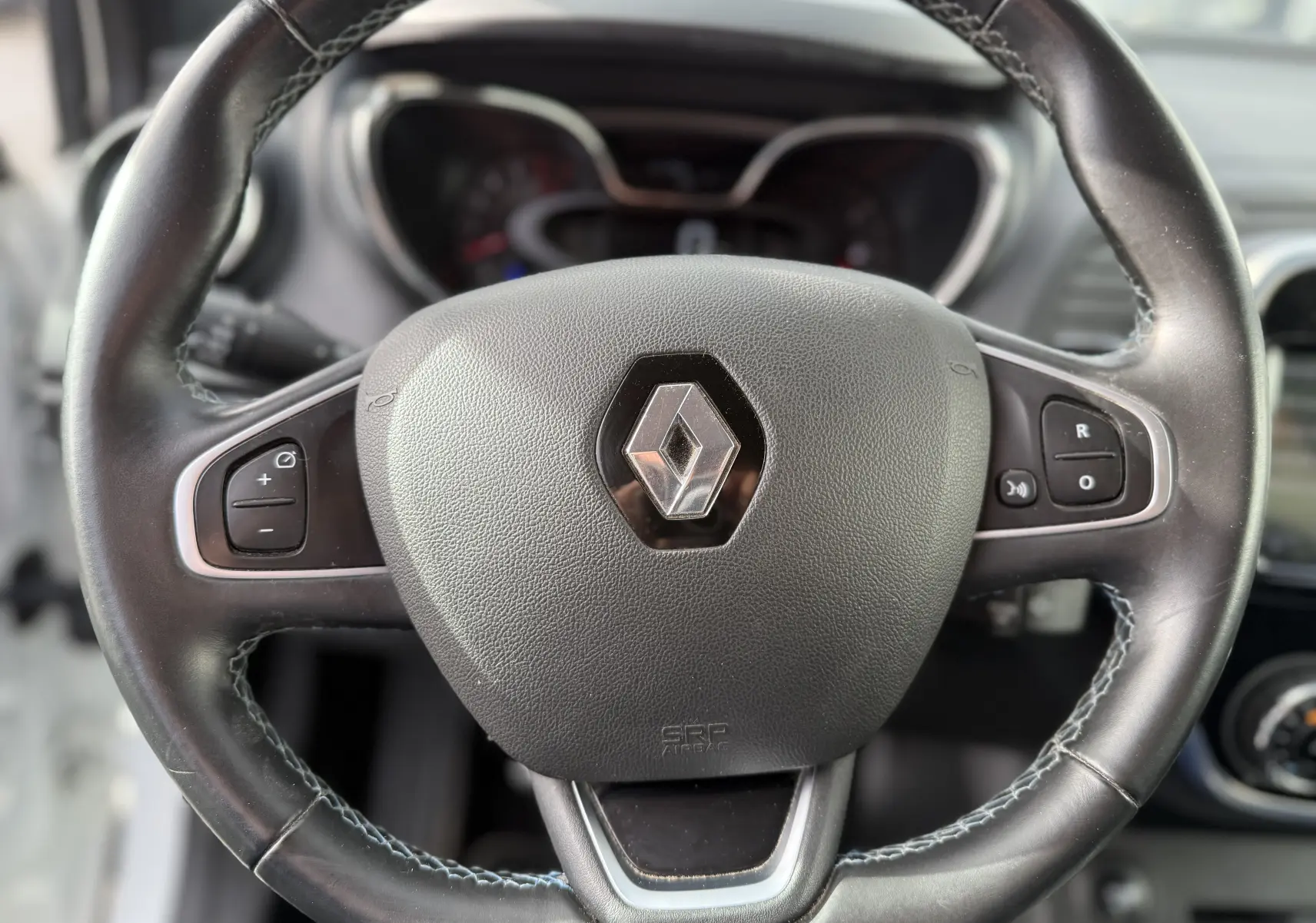 Gros plan sur le volant en cuir noir avec logo Renault au centre du Renault Captur blanc de 2017.