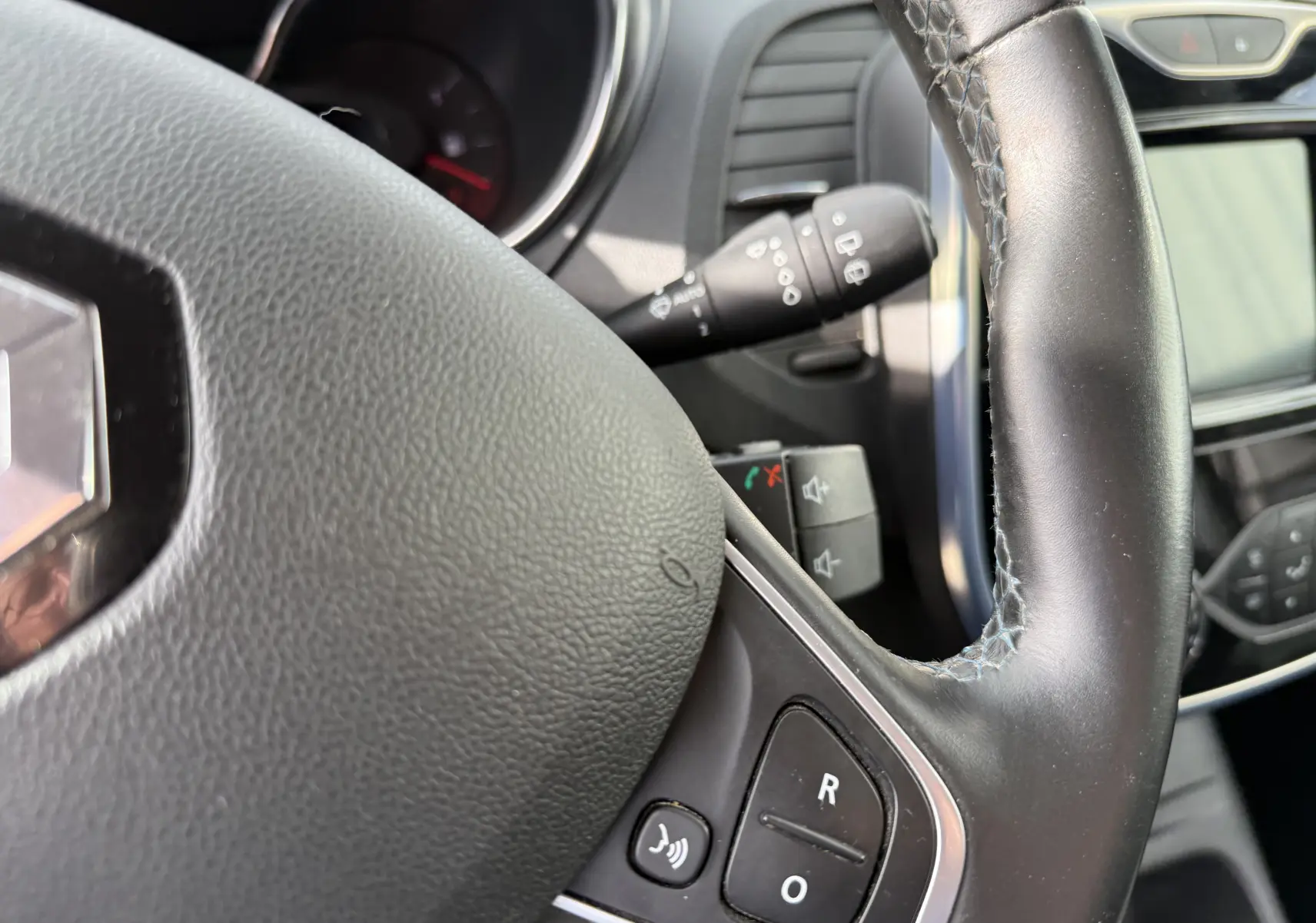 Gros plan sur le volant en cuir noir du Renault Captur blanc 2017, avec commandes intégrées et tableau de bord partiellement visible.