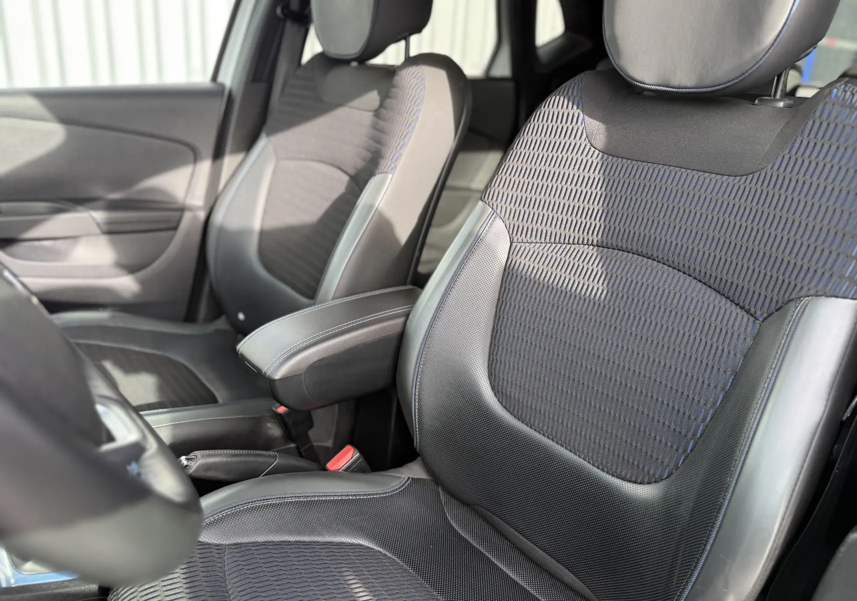 Gros plan sur les sièges avant noirs et bleus du Renault Captur 2017, avec accoudoir central et détails en cuir.