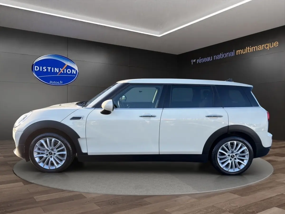 Vue de profil côté gauche d'une MINI Clubman Cooper Exquisite blanche avec jantes alliage et protections noires.