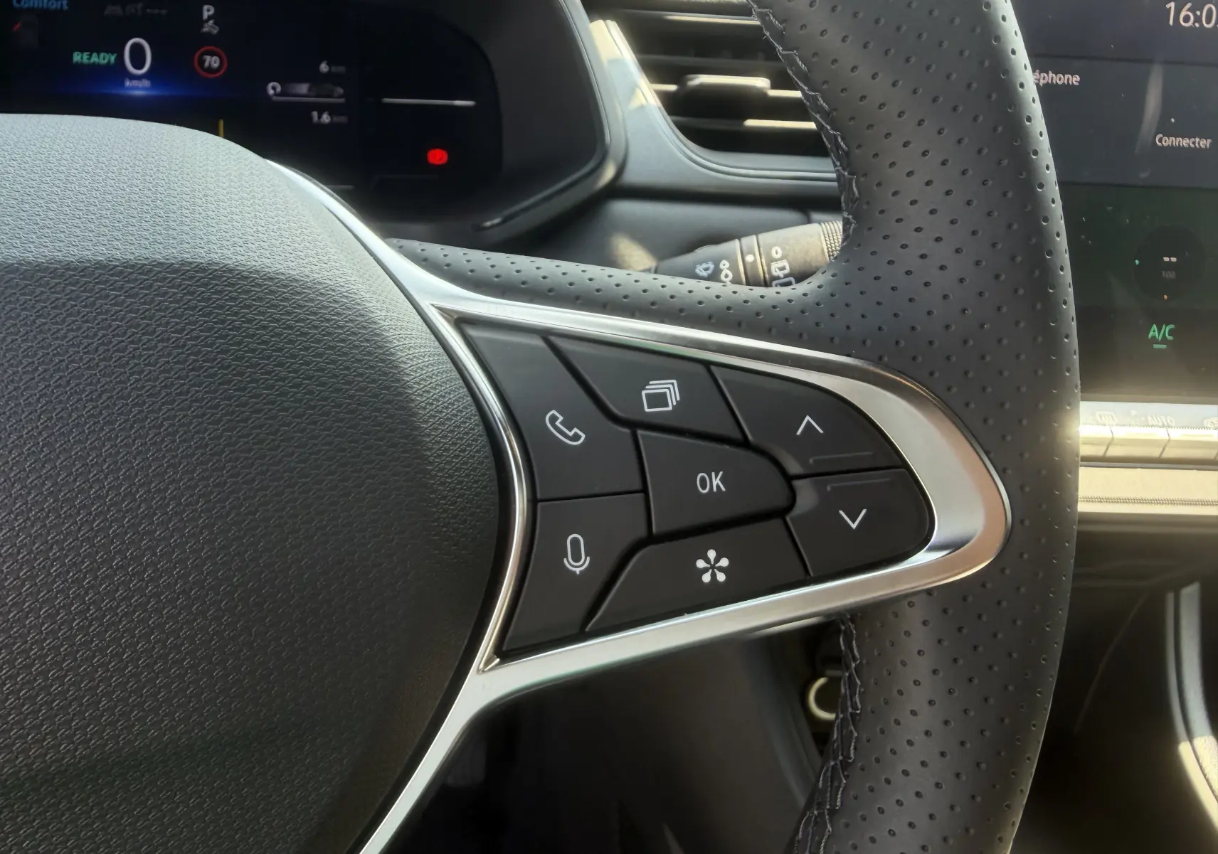 Gros plan sur le volant textile perforé côté droit du Renault Captur 1.8 E-Tech gris Cassiopée, avec commandes multifonctions.