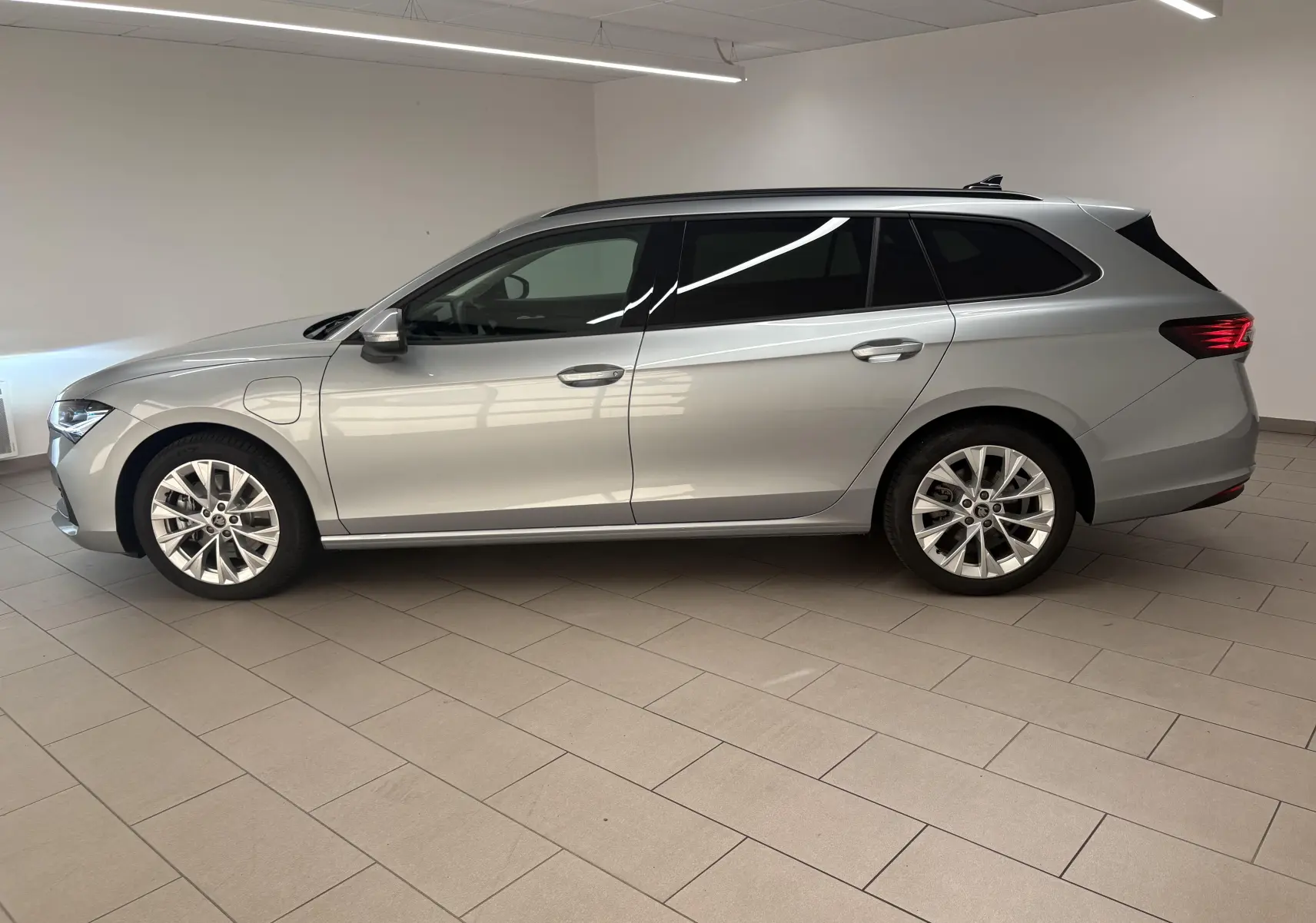 Vue de profil côté gauche d'une Skoda Superb Combi gris argent avec jantes alliage 18 pouces en intérieur showroom.