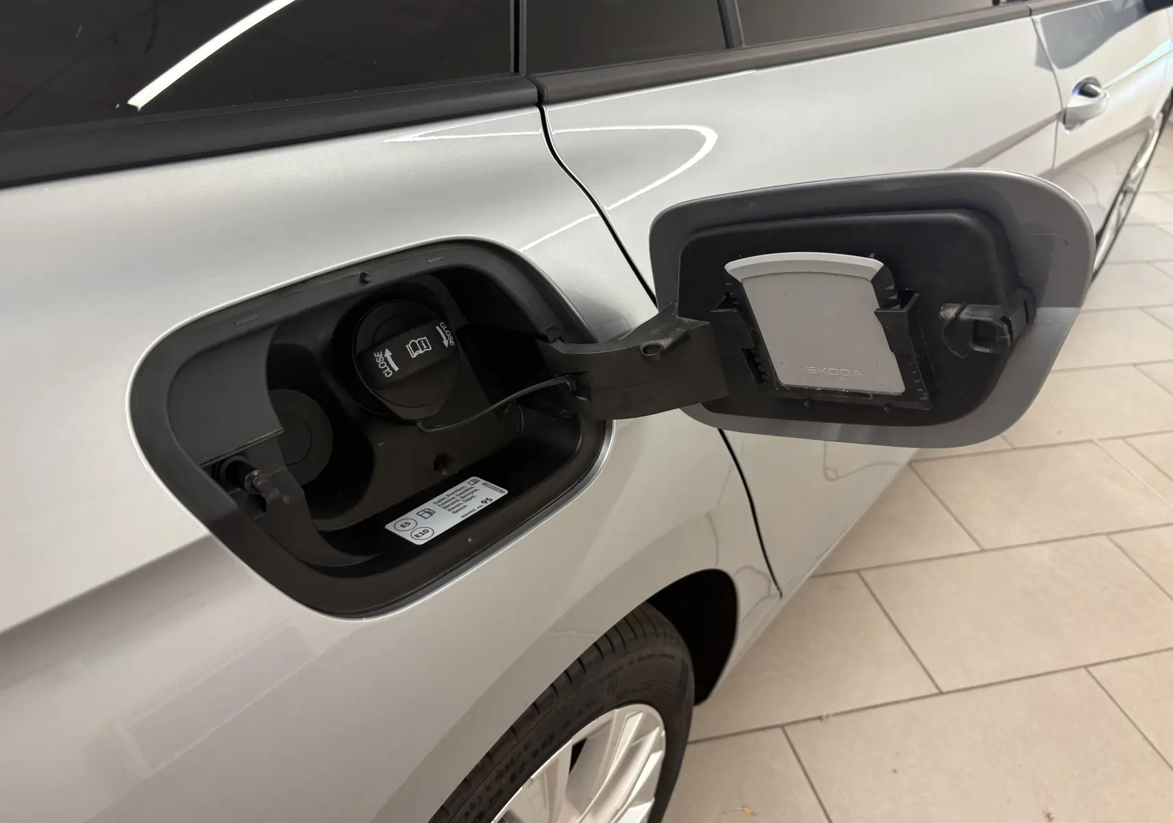 Vue rapprochée du côté gauche du Skoda Superb Combi gris argent, montrant la trappe de recharge hybride ouverte.