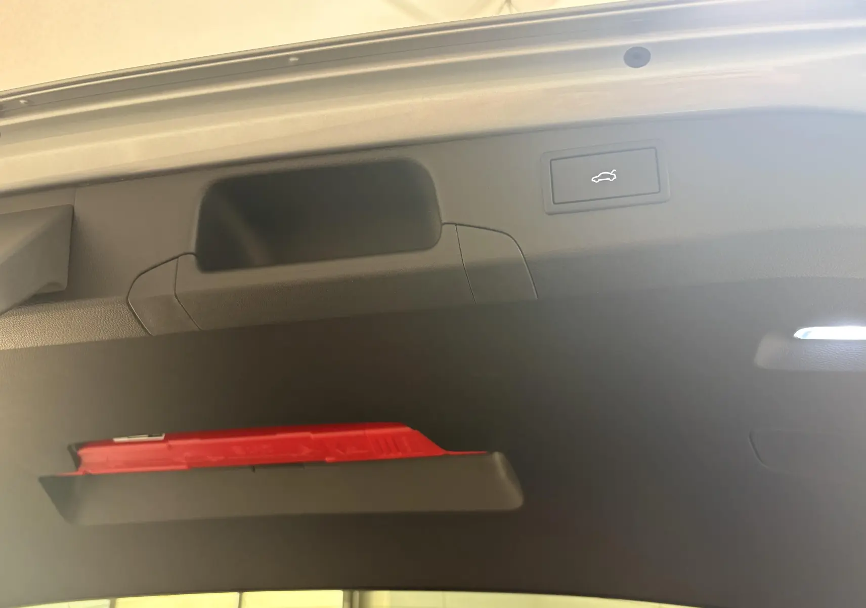Détail du hayon intérieur du Skoda Superb Combi gris argent, montrant le bouton d'ouverture électrique et un triangle de sécurité rouge.