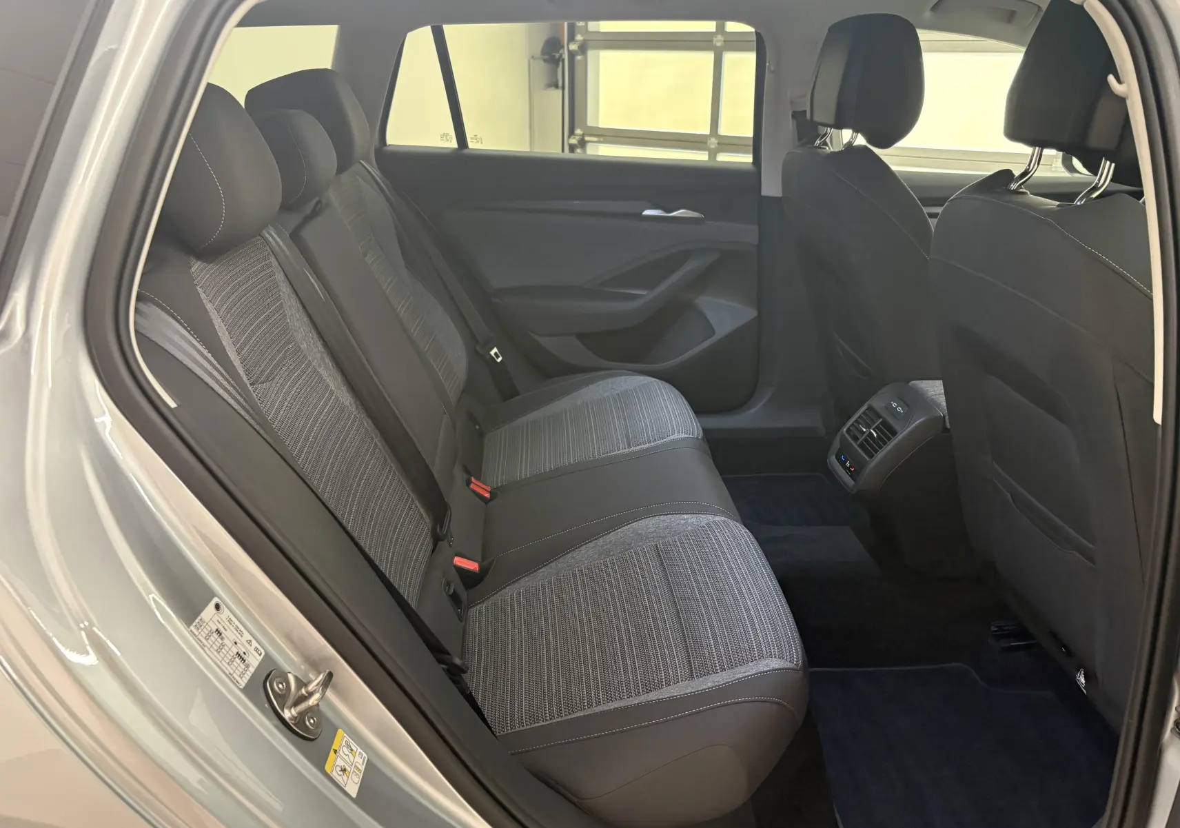 Vue intérieure arrière côté gauche de la Skoda Superb Combi gris argent, montrant les sièges arrière en tissu et cuir avec ventilation centrale.