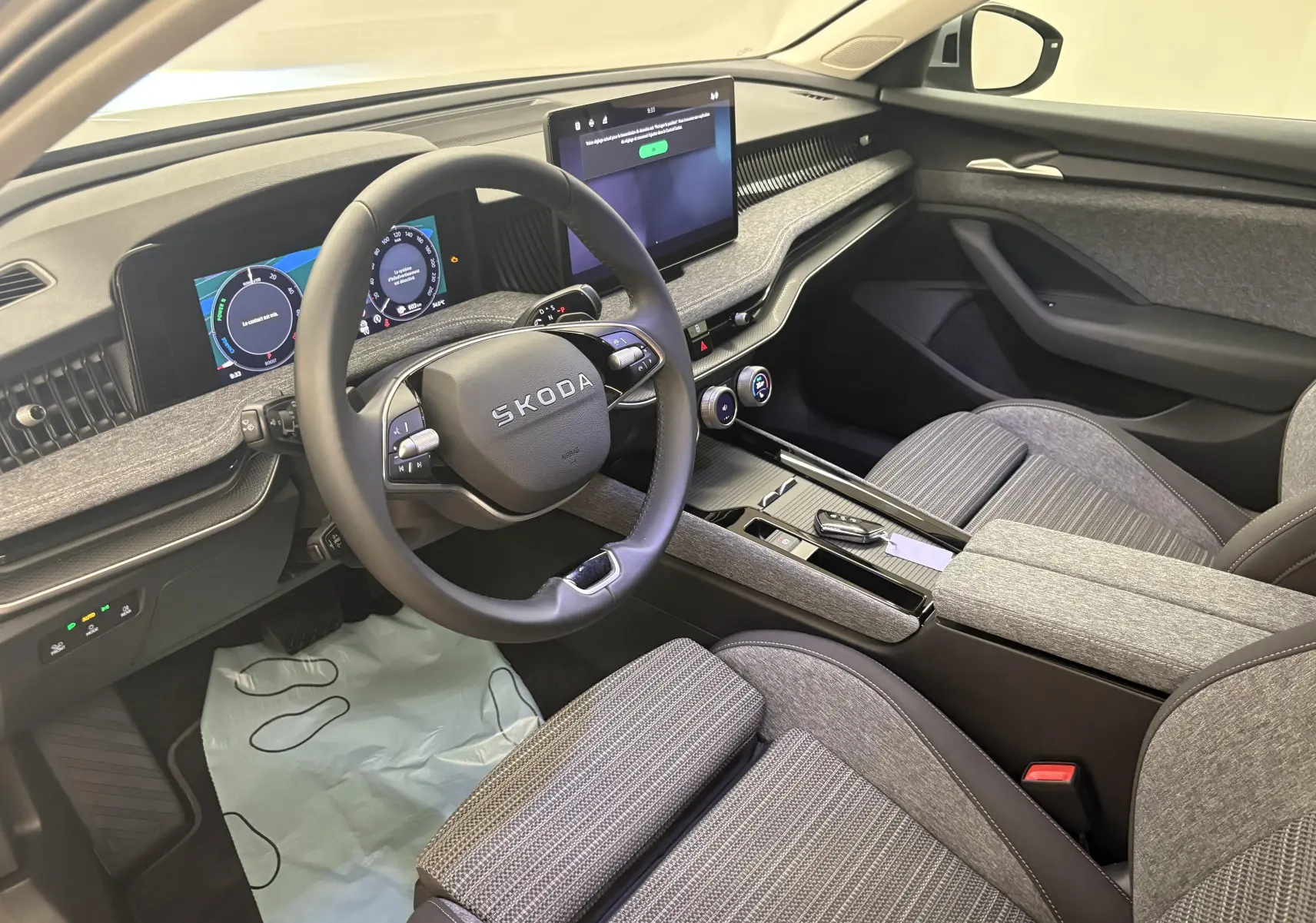 Vue intérieure côté conducteur de la Skoda Superb Combi 2025, tableau de bord gris clair avec écran tactile central et volant multifonction.