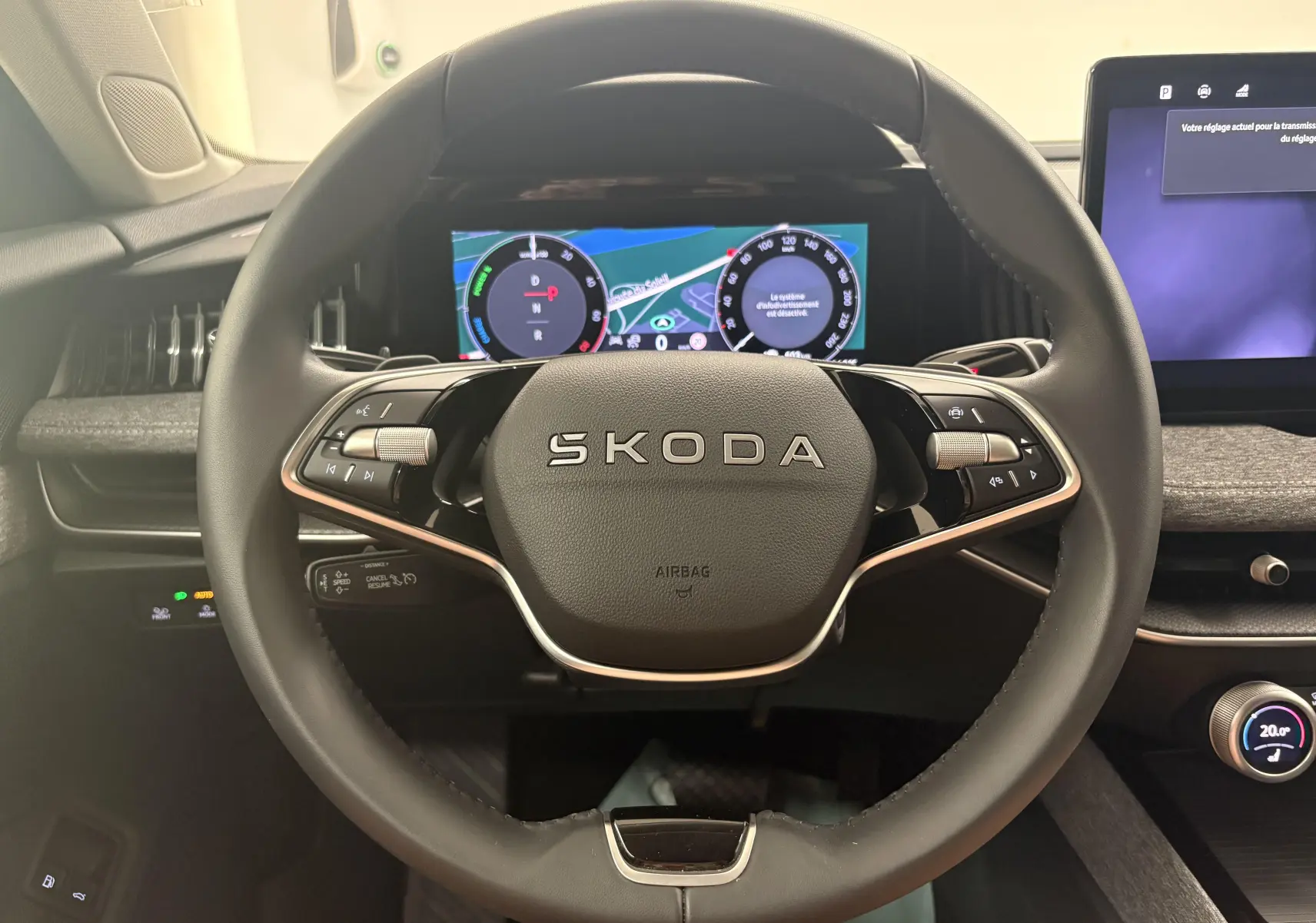 Vue rapprochée du volant SKODA noir avec logo central et tableau de bord numérique lumineux en arrière-plan.